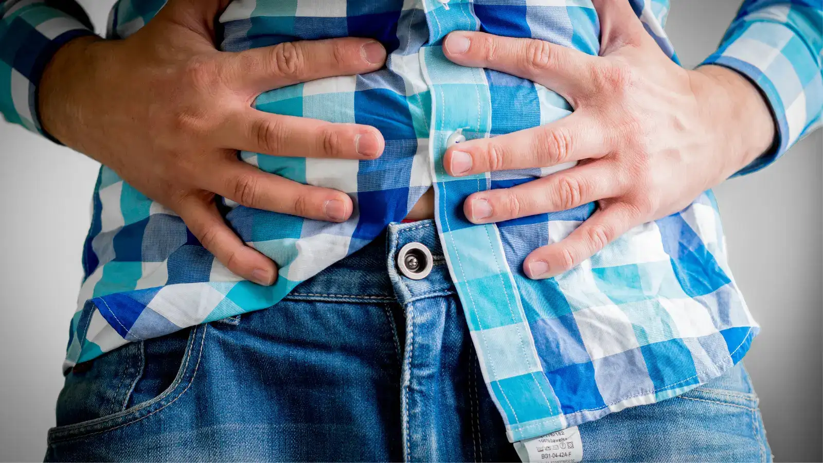 A man in a checked shirt holding his bare stomach with both hands