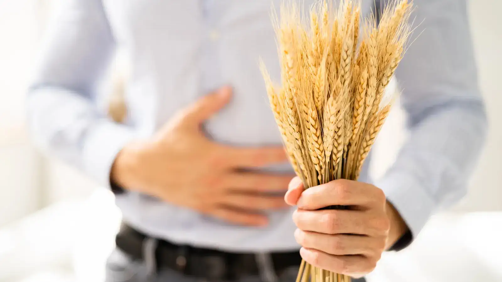 A man holding a bunch of wheat ears against his stomach, his other hand on his abdomen