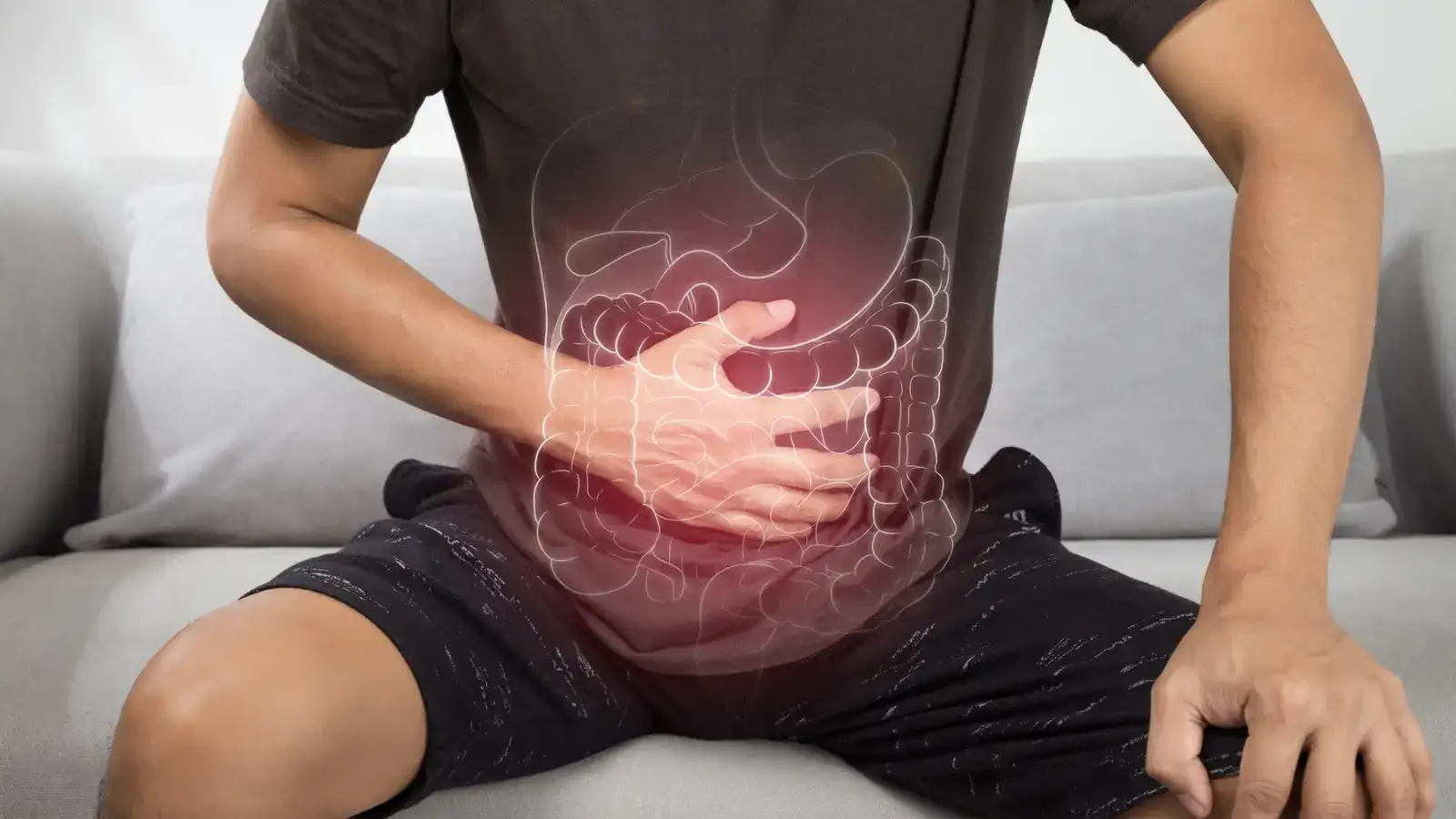 A man sitting on a sofa holding his stomach, the intestines drawn over his abdomen and glowing red