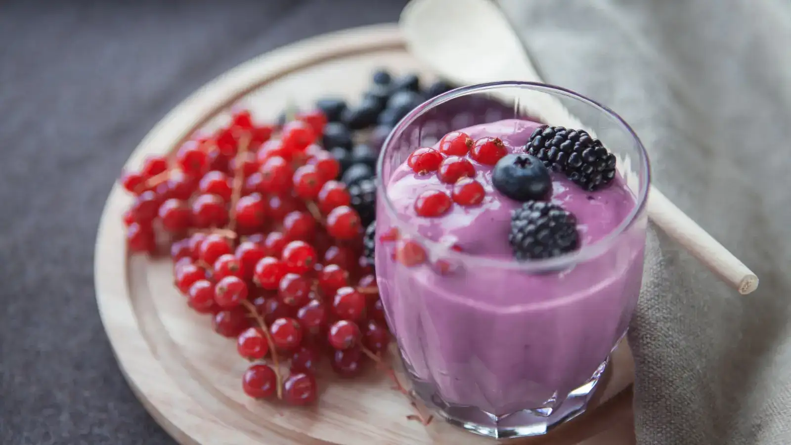 A glass of berry smoothie on a wooden board beside redcurrants and blackberries