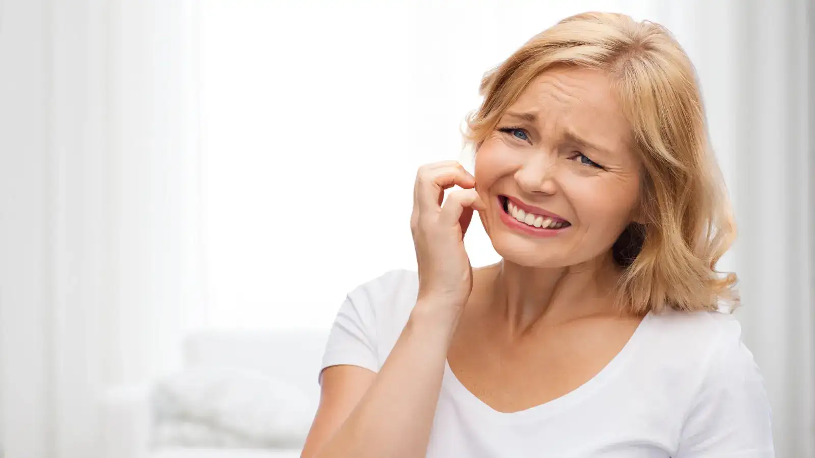 A woman wincing as she touches the side of her face