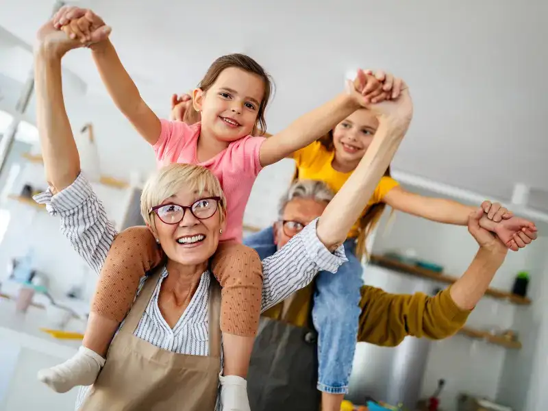 A grandmother and two girls dancing together with their arms raised in a kitchen