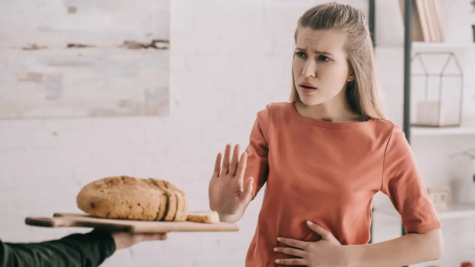 A woman raising a hand to refuse a board of bread, her other hand resting on her stomach