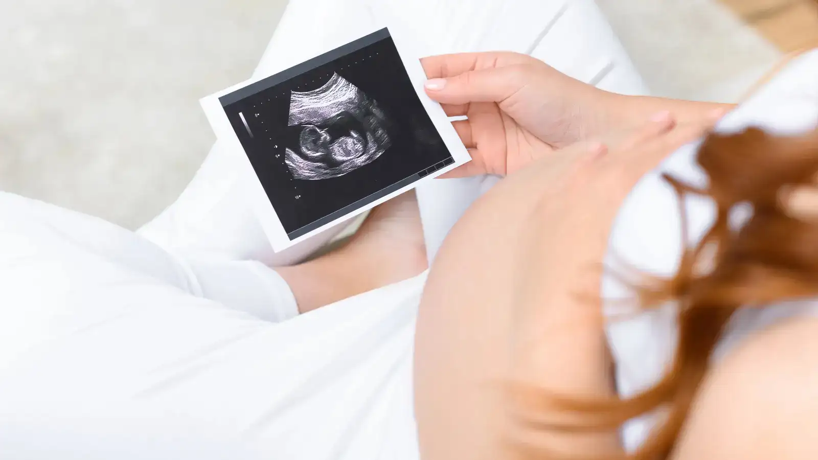 A pregnant woman looking at an ultrasound scan on a tablet resting on her bump