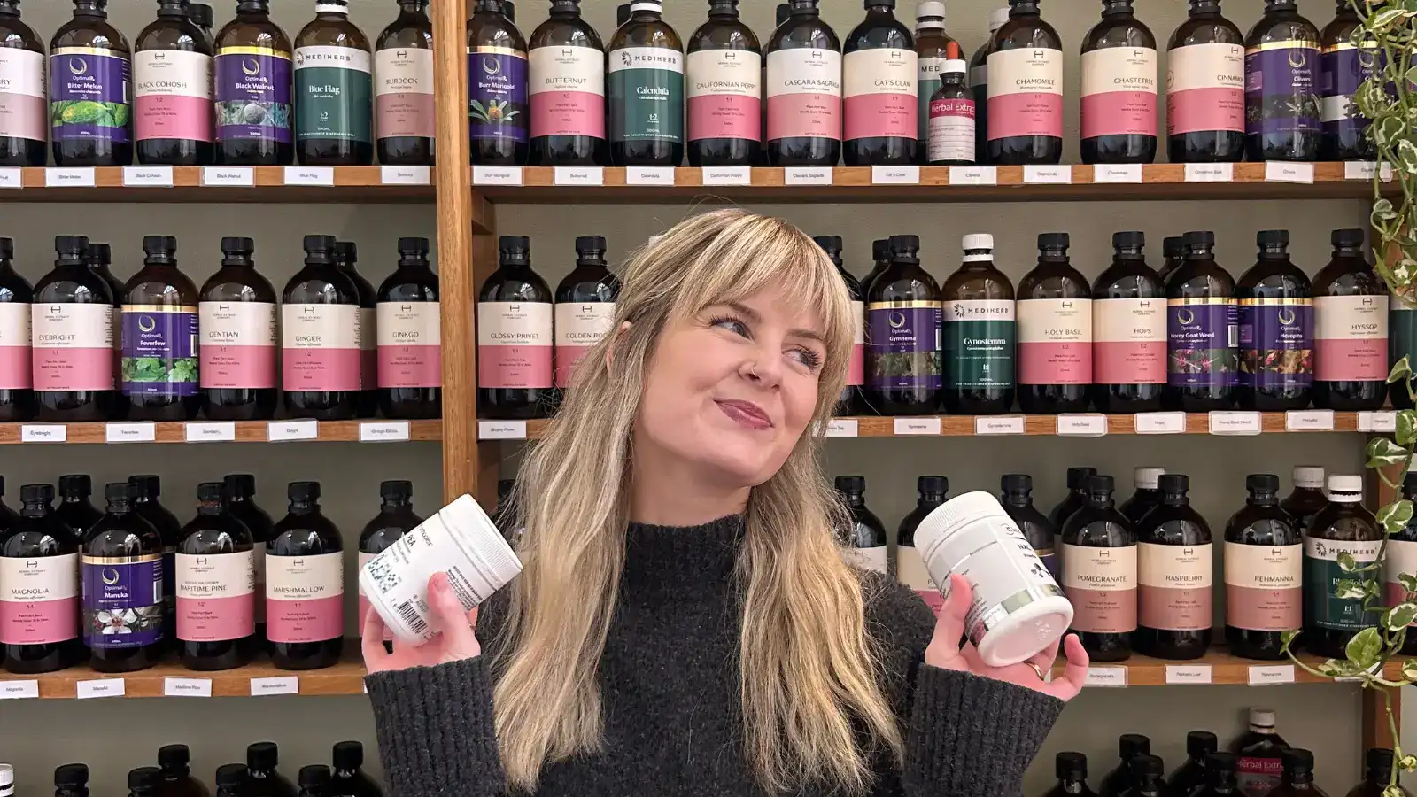 A naturopath at the dispensary shelves, holding two supplement bottles