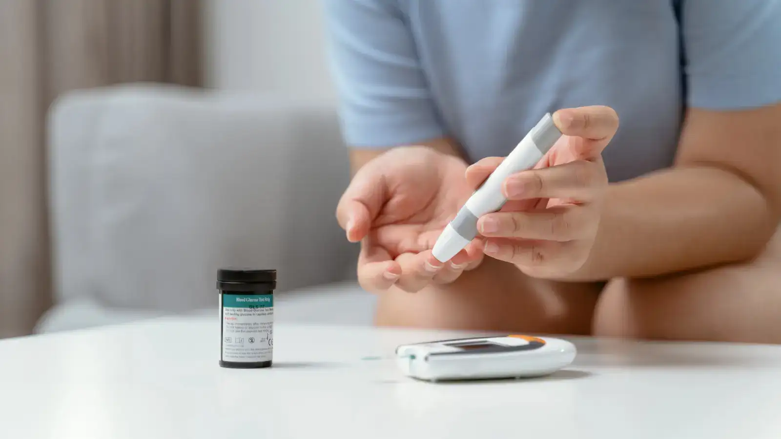 A person pricking a finger for a blood glucose test beside a meter on a table