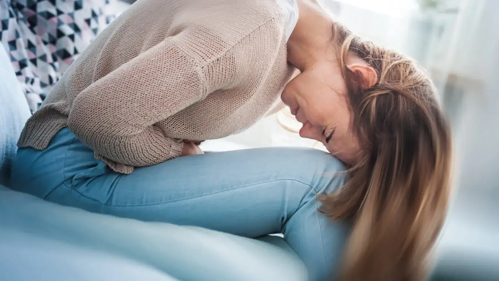 A woman curled forward on a bed holding her lower abdomen