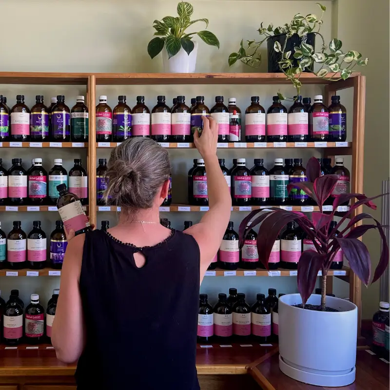Naturopath selecting herbal extract tinctures from a fully stocked dispensary shelf at a Melbourne herb clinic