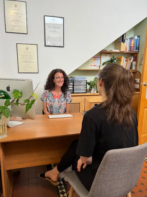 Naturopath consulting with a patient at her Brunswick clinic desk, with university qualifications displayed on the wall