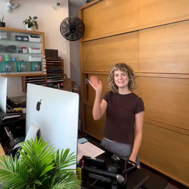Smiling receptionist waving welcome at the front desk of a Melbourne naturopathy clinic reception area