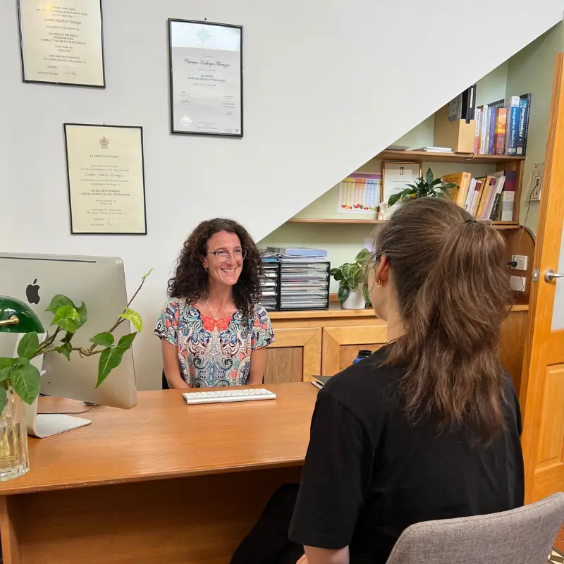 Naturopath consulting with a patient at her Brunswick clinic desk, with university qualifications displayed on the wall