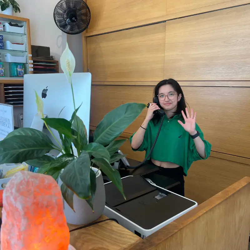 Friendly receptionist waving at the front desk of a Melbourne naturopathy clinic with a Himalayan salt lamp